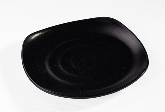 Black ceramic plate with rounded square shape and subtle concentric ridges, isolated on white background with soft shadow
