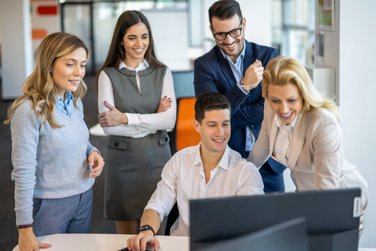 Group of business colleagues gathering around desktop computer monitor to celebrate project success.