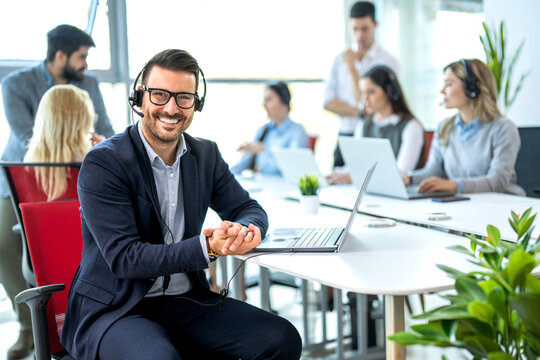 Call center representative wearing headset sitting at desk with laptop in open space office.