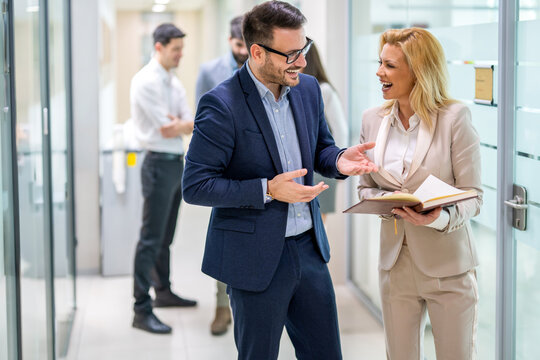 Smiling businessman and businesswoman discussing notes in modern office hallway