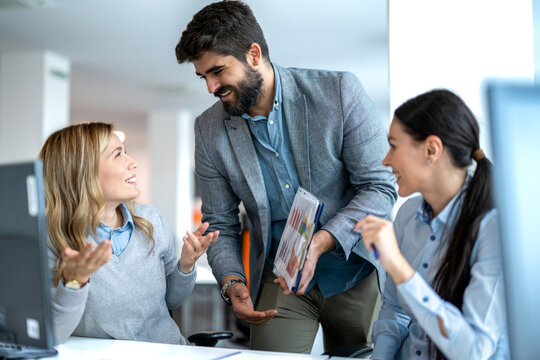 Businessman showing chart folder to two female colleagues sitting at office desk