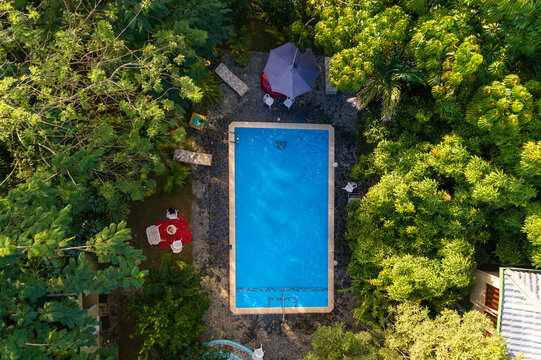 Aerial view of the swimming pool at Loma Linda, surrounded by lush green trees, a patio area with a red tablecloth, and a parasol in Pedro Brand, Santo Domingo Provinc, Dominican Republic.