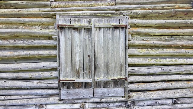 Close-up of an old weathered wooden hut with closed wooden shutters in the Swiss Alps. The aged timber, rustic facade and traditional details create an authentic alpine character.