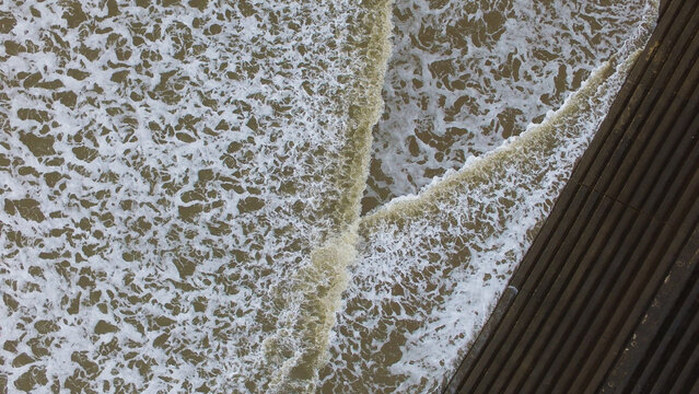 Aerial view of waves crashing against a wooden boardwalk at Three Cliffs Bay, United Kingdom.