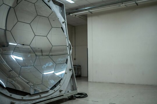 Hexagonal mirror segments catching fractured reflections inside an observatory workshop