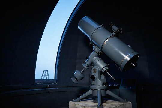 Reflecting telescope on an equatorial mount inside an open dome at blue dusk