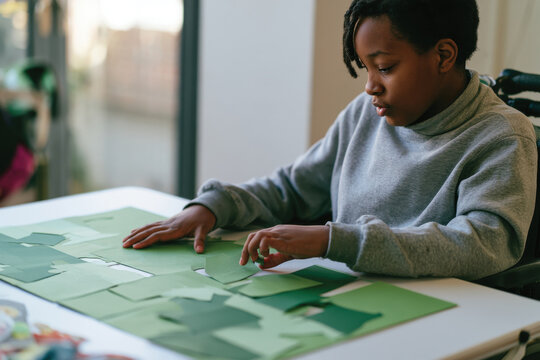 A young girl works meticulously on a green paper crafting project, highlighting her focus and skill development, representing creativity and personal expression in an art setting.