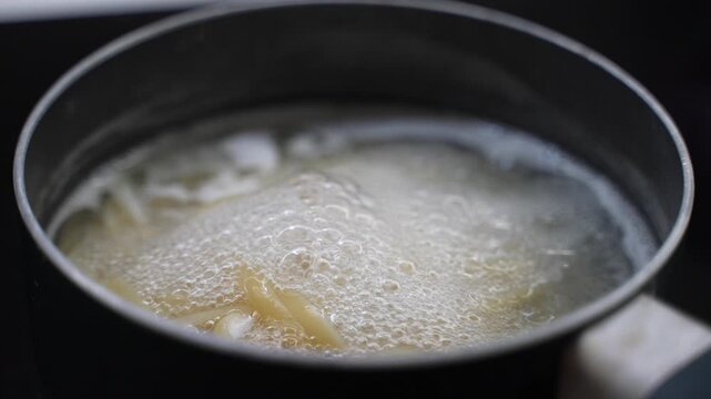 Close up of pasta boiling in water inside a metal pot, with rising bubbles and steam during cooking.