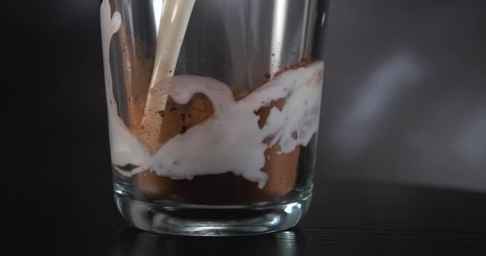 Milk pouring into cocoa powder in a glass slow motion black background