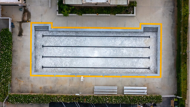 Aerial view of a rectangular swimming pool with lane markers, surrounded by concrete decking, benches, and lush green hedges in Baldwin Hills, Los Angeles, California, United States.
