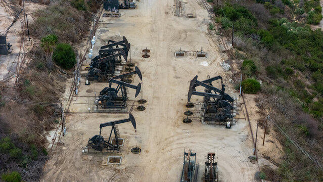 Aerial view of oil pump jacks operating in the Baldwin Hills oil field surrounded by dry terrain and vegetation in Los Angeles, California, United States.