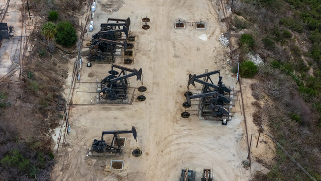 Aerial view of oil pumpjacks operating in the Baldwin Hills oil field, surrounded by dry terrain and sparse vegetation in Los Angeles, California, United States.