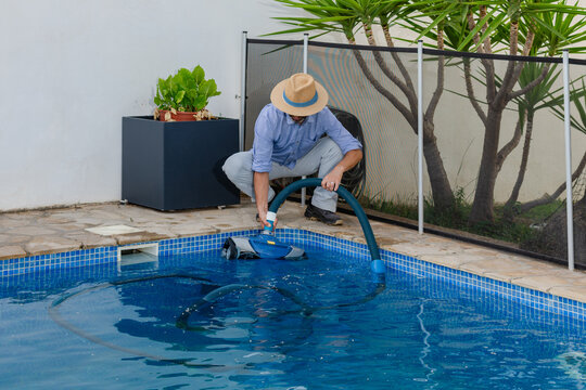 Pool maintenance worker crouching beside swimming pool using cleaning machine