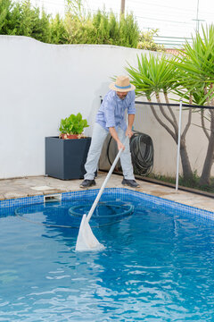 Vertical pool maintenance worker removing debris from swimming pool with skimmer net
