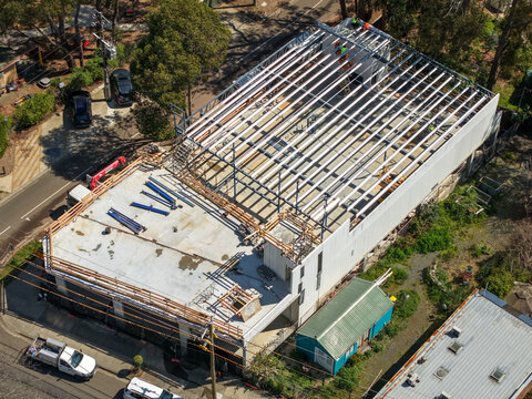 The Basin, Australia - 18 September 2026: Aerial view of a building under construction showing exposed steel roof beams, concrete flooring, and workers on site.