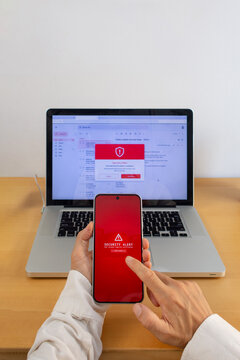 Hands holding smartphone with security alert and laptop email warning