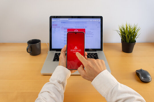 Smartphone security warning with laptop showing suspicious email alert