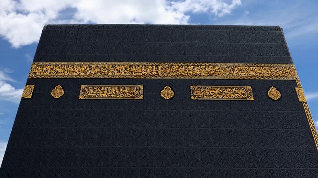Close up view of the Kaaba at Masjid al Haram in Mecca, Saudi Arabia, featuring its black Kiswah with intricate golden Arabic calligraphy and the Makkah Royal Clock Tower in the background