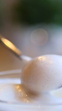 Creamy dessert mousse swells on spoon with gentle motion. White topping domes and narrows over shallow dish, showing silky texture, soft highlights, and luxurious food presentation.