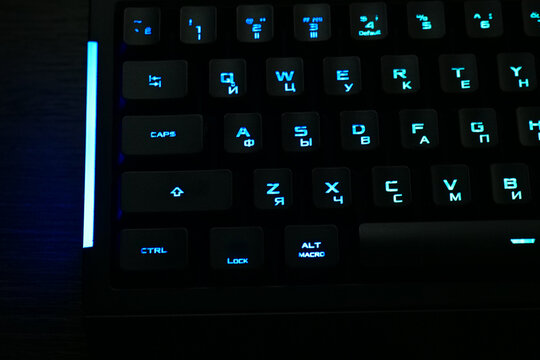 black gaming mechanical keyboard with blue led backlight close up, illuminated computer keyboard with cyrillic letters in darkness, macro shot of backlit gaming keyboard keys with blue light