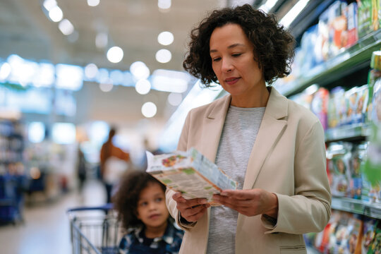 A mother is checking food labels with her child sitting in the shopping cart, representing family life and the importance of healthy food choices in daily routines.