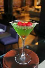 Green Cocktail in Martini Glass Garnished with Red Maraschino Cherries on Skewer and Basil Seeds © Rara