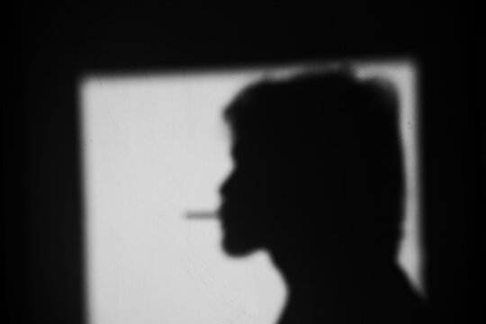 Close up side view black and white shadow of a man smoking cigarette on the dirty wall