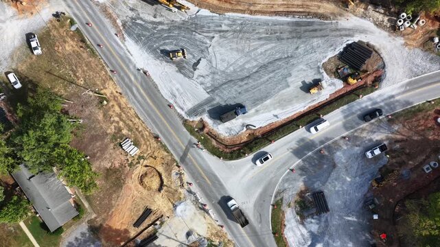 A graded stone pad, stacked drainage pipe and concrete structures fill a road construction site at Lynchburg, Virginia, traffic passing on the one open lane. Aerial top down flyover