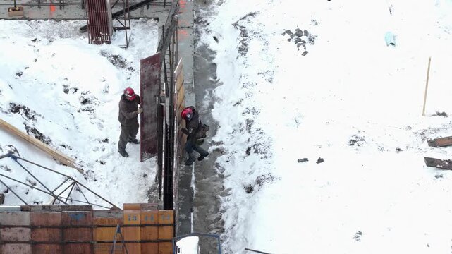 Workers Installing Concrete Wall Formwork on Snowy Site