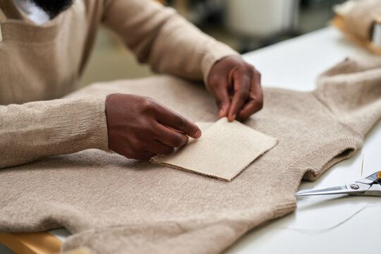 A focused artisan attaches a fabric patch onto a sweater in a bright studio, blending modern techniques with traditional approaches to clothing repair and customization.