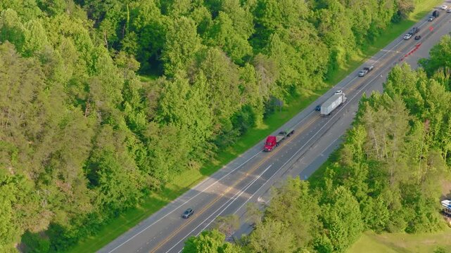 Semi truck flatbed aerial drone view over Interstate 40 in Tennessee: a red big rig with a strapped cargo load rolls past orange construction barrels as cars pass in the far lanes.