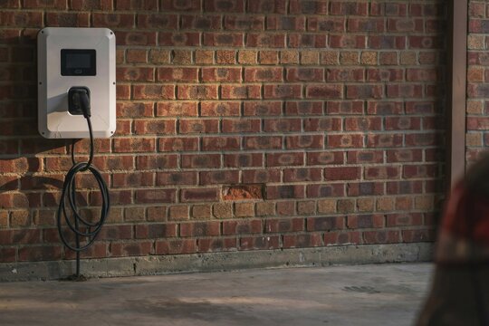 Wall mounted home charge point and coiled cable in a dim residential garage at dusk