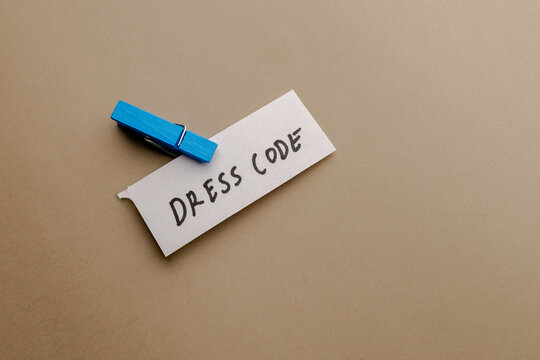 A note with text dress code attached by a blue clothespin on a brown background, minimalist office concept for corporate policy and style