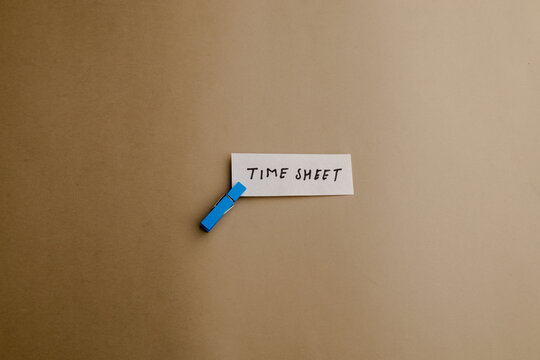 Time sheet note clipped with blue peg on brown background, concept for business office workflow, employee attendance and job schedule track