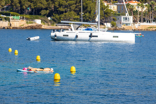 Couple Relaxing on Paddleboard in Calm Mediterranean Sea with Sailing Yacht and Coastal Villas