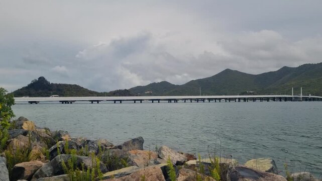 Panoramic view over Simpson Bay, Sint Maarten, with the Simpson Bay Lagoon Causeway Bridge, tropical hills, and lush island landscape beneath a cloudy overcast sky
