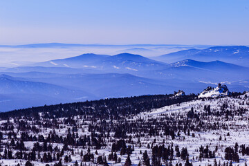 Obraz premium Panoramic view of mountain ridges covered morning mist and blue pink pastel colored sky. Distant peaks fade smoothly in horizon, creating depth effect under clear winter sky. Scenic landscape.