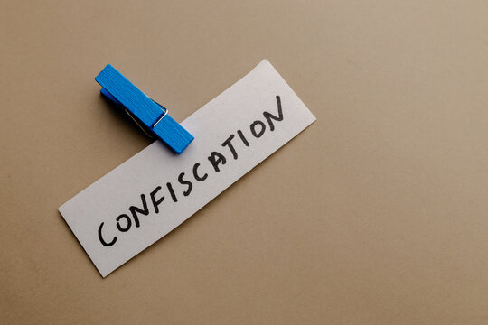 A close up view of a paper note with text confiscation attached with a blue wooden clip on a neutral background for business conceptual use