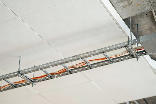 Galvanised cable tray carrying orange and white leads through a ceiling void