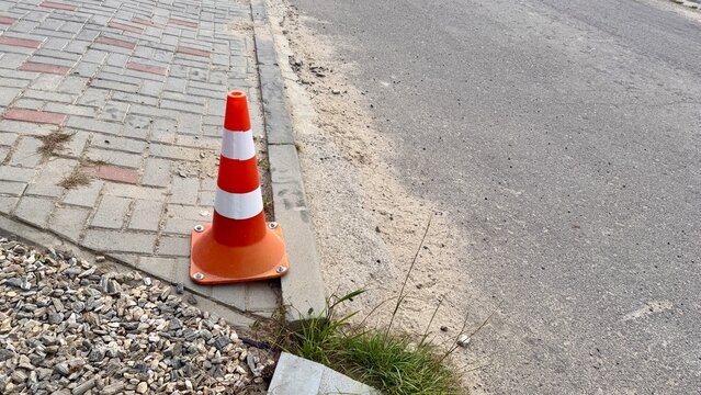 Orange traffic cone on sidewalk near asphalt road