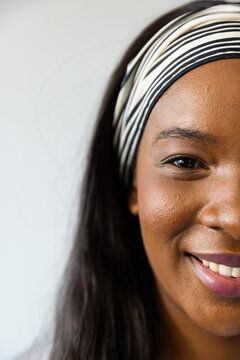 African woman smiling, showing mauve lips with striped headband against pale wall, copy space