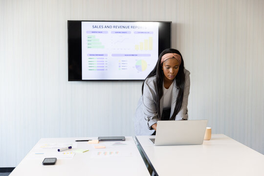 African American woman leaning on laptop at table wearing grey blazer viewing sales data