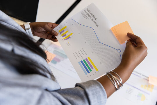 Female professional wearing gray blazer holding and examining chart on white table with sticky note