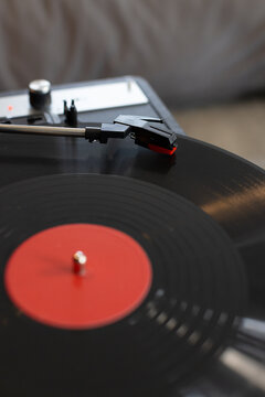 Black vinyl record spinning on turntable with tonearm lowering cartridge and red stylus