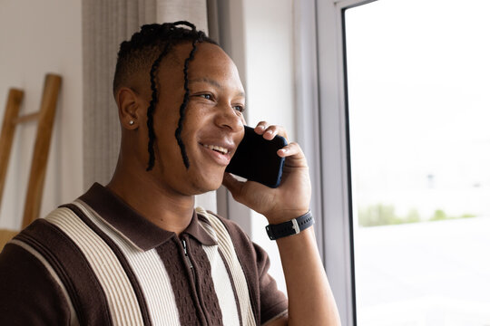 Adult man standing by large window holding phone to right-ear, in striped polo, watch, stud earring