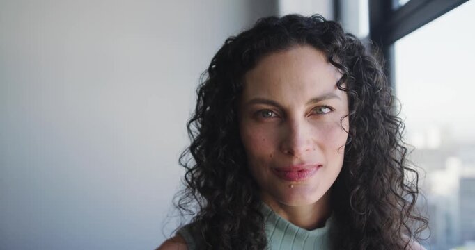 African American woman by large window making eye contact then smiling, showing nose, lip studs