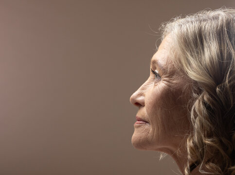 Senior woman posing in strict profile at studio showing face gray hair neutral backdrop, copy space