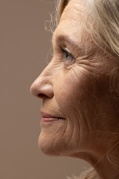 Senior female facing right in studio portrait, showing wrinkles, stray hairs, mascara on lashes