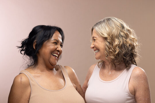 Diverse female friends with senior woman laughing facing one another in studio wearing tank tops