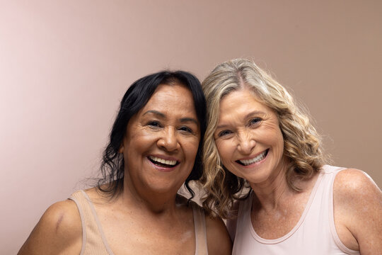 Senior and mature female friends wearing sleeveless tops posing in studio with neutral backdrop